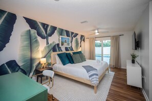 A hotel room with a bed, a desk, a chair, a TV, and a view of the sea. - Epic Yard Movie Theater Pool Arcade Games (Seminole)