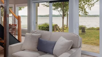 A room with a beige sofa, a wooden staircase, and a view of a lake through large glass doors.