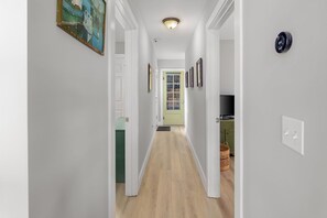 A hallway with a wooden floor, white walls, and a green door at the end. - Gorgeous Lakefront Home w Private Beach Views (South Burlington)