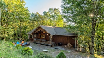A cabin with a porch, surrounded by trees, and outdoor seating.