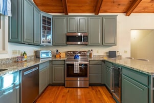A kitchen with a stainless steel microwave, oven, and dishwasher, wooden cabinets, and a granite countertop.