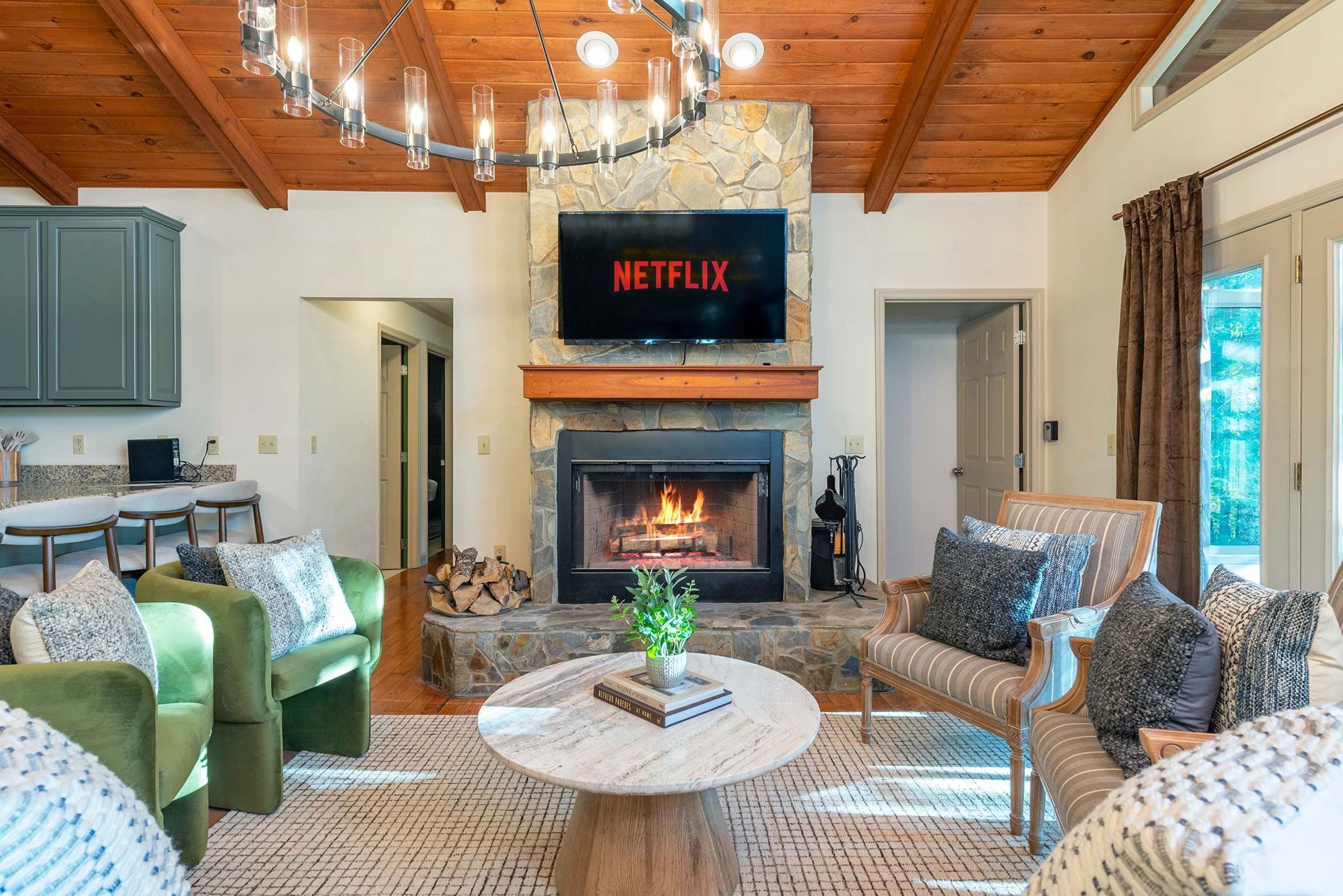 A living room with a stone fireplace, a television mounted above it, and a chandelier.