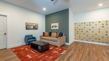 A living room with a sofa, a coffee table, a blue chair, a red rug, and a climbing wall.