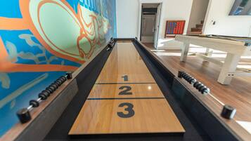 A shuffleboard table with numbered ends, a pool table, and a colorful mural in the background.