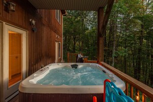 A hot tub on a wooden deck with a view of a forest.