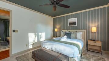 A bedroom with a bed, a ceiling fan, two bedside lamps, a nightstand, a bench, and a framed picture on the wall.