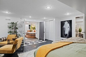 Une chambre moderne avec un grand lit, un coin salon avec des fauteuils, un tableau représentant un cheval et une vue sur une salle de bain.