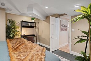 Ein Zimmer mit Bett, Schreibtisch, Stuhl, Pflanze und einer Tür.