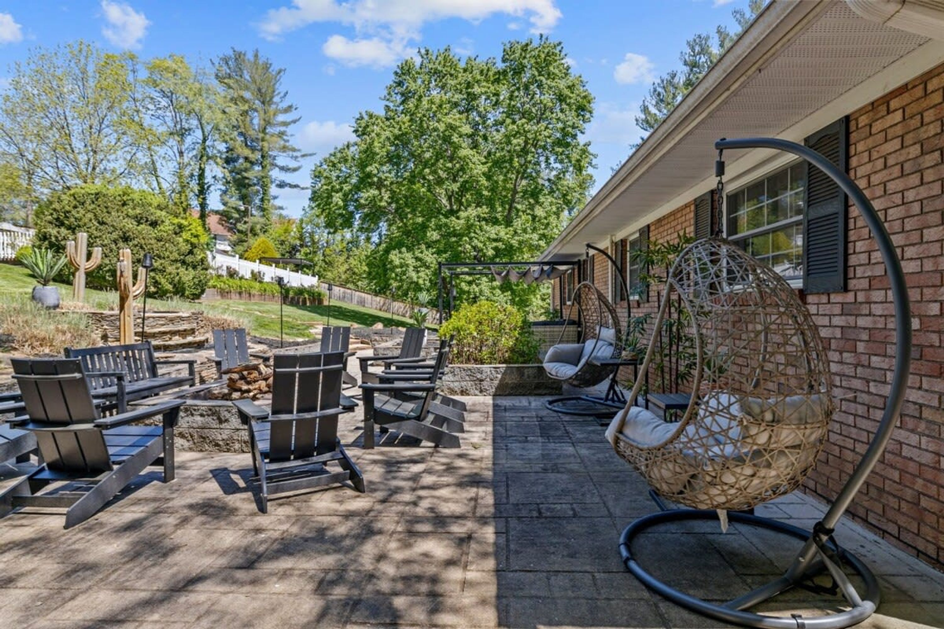 Une terrasse extérieure avec des fauteuils Adirondack, un fauteuil suspendu et un mur en briques.