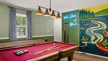 A pool table with cues and balls, a neon sign, and a mural of a river scene.