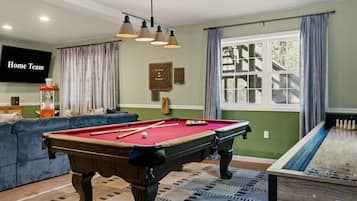 A pool room with a pool table, a billiards table, a sofa, and a television.