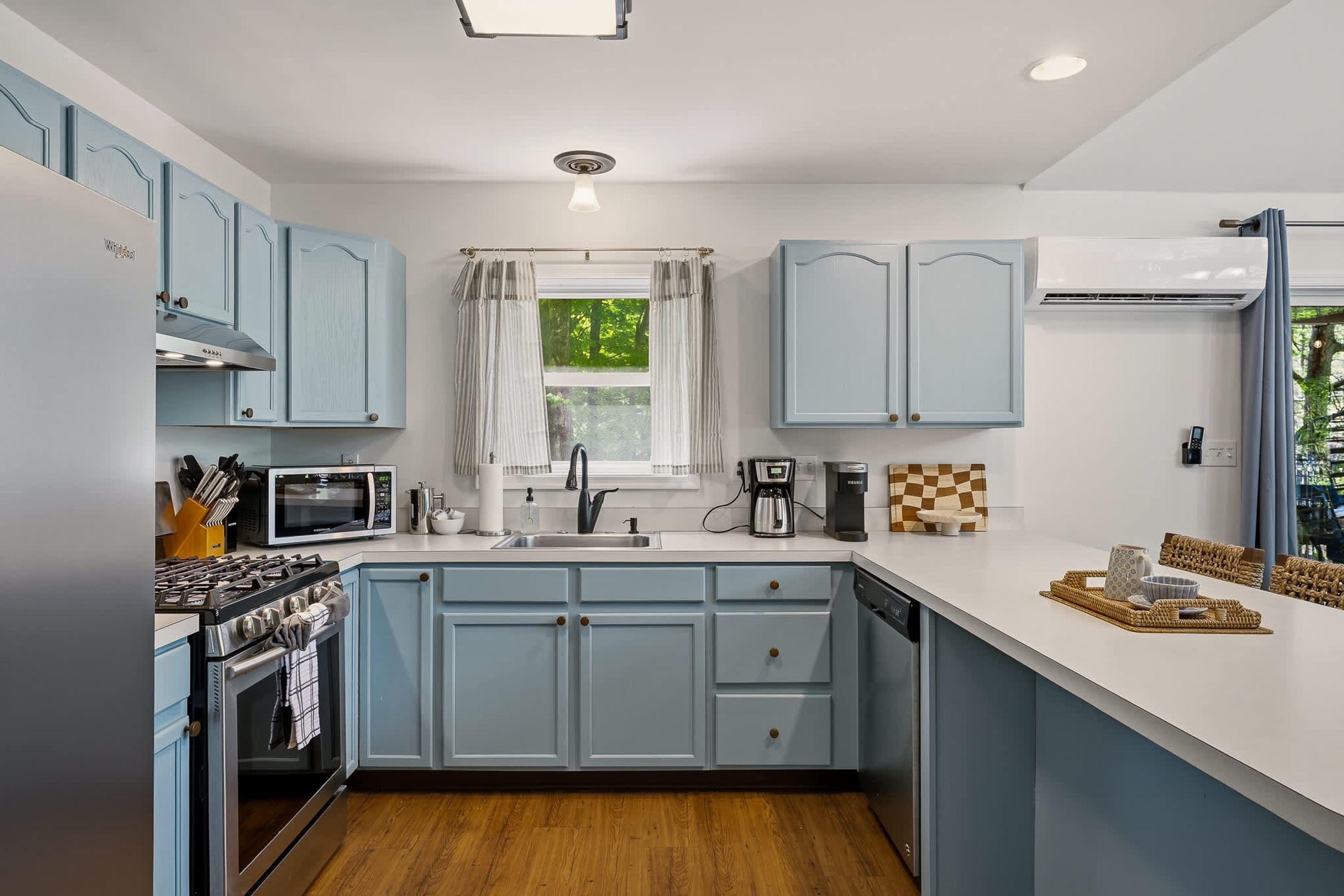 A kitchen with light blue cabinets, a microwave, a coffee maker, and a window with curtains.