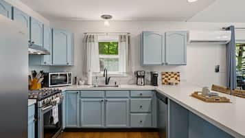 A kitchen with light blue cabinets, a microwave, a coffee maker, and a window with curtains.