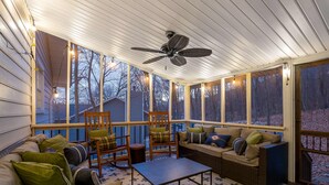 Un solarium con ventilador de techo, ventanas amplias y una zona de estar con sofá y sillones.