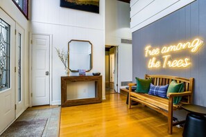 A hallway with a wooden bench, a mirror, and a neon sign that reads 'Free among the Trees.' - Cozy Retreat - Sauna Hot Tub Pool Pass Game Room (McGaheysville)