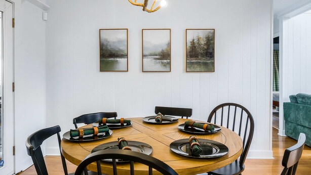 Un comedor con una mesa redonda de madera, sillas negras y una araña.