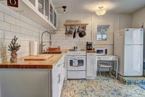 A compact kitchen with white cabinets, a wooden countertop, a sink, a stove, a microwave, and a refrigerator. - Sunshine Cottage- Fire Pit Fenced in Yard (Port Aransas)