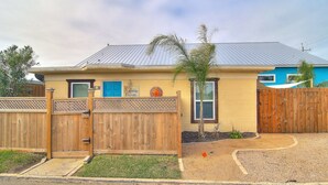 A two-story house with a fenced front yard, a blue door, and a small tree. - Sunshine Cottage- Fire Pit Fenced in Yard (Port Aransas)