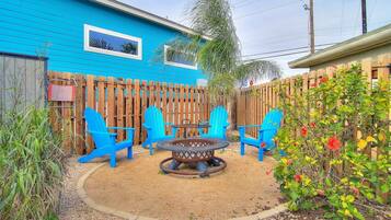 Un patio trasero con una casa azul, una valla de madera y muebles de exterior, como sillas y una mesa.