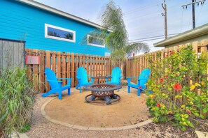 Ein Garten mit einem blauen Haus, einem Holzzaun und Gartenmöbeln, darunter Stühle und ein Tisch.