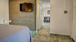 A hotel room with a bed, a television mounted on a wooden wall, a small table, and a door leading to another room. - Sunshine Cottage- Fire Pit Fenced in Yard (Port Aransas)