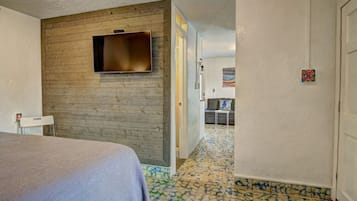 Habitación de hotel con cama, televisor montado en una pared de madera, una mesita y una puerta que da a otra habitación.