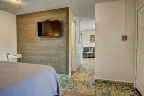 Ein Hotelzimmer mit einem Bett, einem an einer Holzwand montierten Fernseher, einem kleinen Tisch und einer Tür zu einem weiteren Raum.