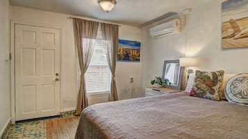 Un dormitorio con cama, ventana con cortinas, aire acondicionado de pared y un cuadro.