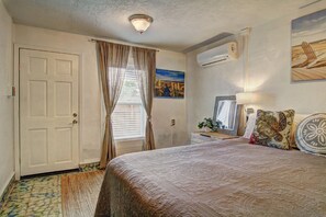 Un dormitorio con cama, ventana con cortinas, aire acondicionado de pared y un cuadro.