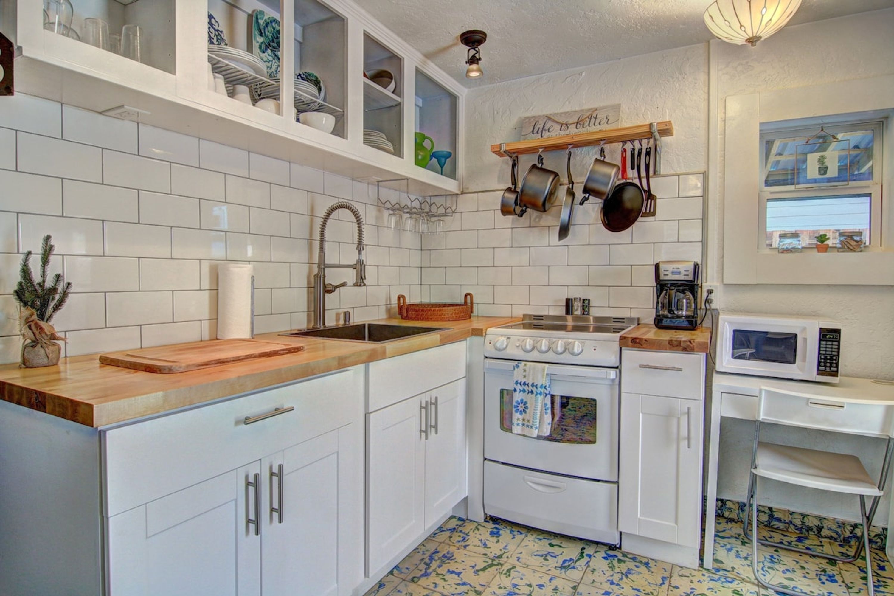 A kitchen with white cabinets, a wooden countertop, a stove, a microwave, and a hanging pot rack.