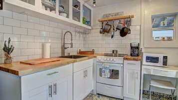 A kitchen with white cabinets, a wooden countertop, a stove, a microwave, and a hanging pot rack.