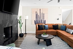 A modern living room with a sectional sofa, a fireplace, a cactus plant, and a large abstract painting on the wall. - Heated Pool Hot Tub Game Room Sport Court (Glendale)