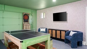 Um quarto com mesa de pingue-pongue, dardos, sofá e televisão.