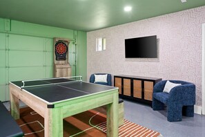 Ein Zimmer mit Pingpongtisch, Dartscheibe, Sofa und Fernseher.