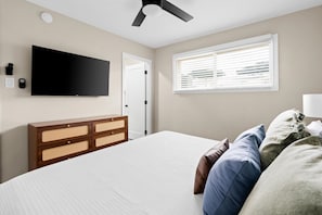 A bedroom with a bed, a television mounted on the wall, a ceiling fan, a window with blinds, and a bedside table with a lamp. - Heated Pool Hot Tub Game Room Sport Court (Glendale)