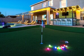 Ein Garten mit Pool, Liegestühlen, Grillplatz und einer Fahnenmasten.