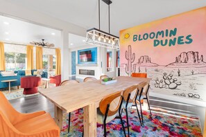 Ein modernes Wohnzimmer mit einem Holzesstisch, bunten Stühlen und einer großen Wandmalerei.