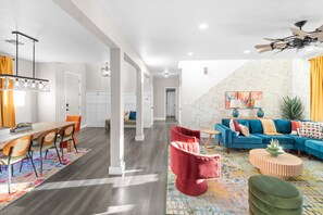 A modern living room with a blue sofa, red armchairs, and a dining area with a wooden table and chairs. - Bloomin Dunes - Pool Pickleball Tiki Bar (Chandler)