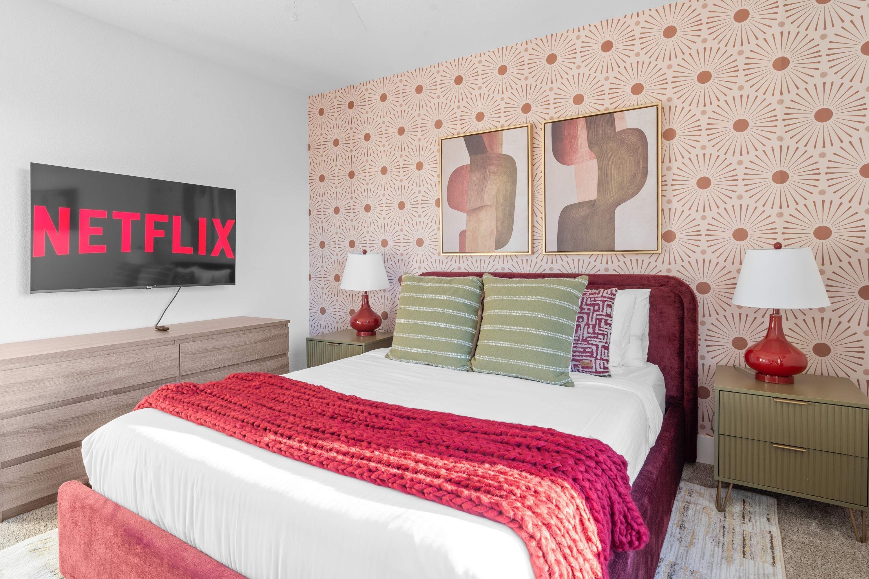 A modern bedroom with a large bed, a TV mounted on the wall, and a patterned wallpaper.