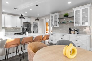 A modern kitchen with white cabinets, stainless steel appliances, and a central island with bar stools. - Bloomin Dunes - Pool Pickleball Tiki Bar (Chandler)