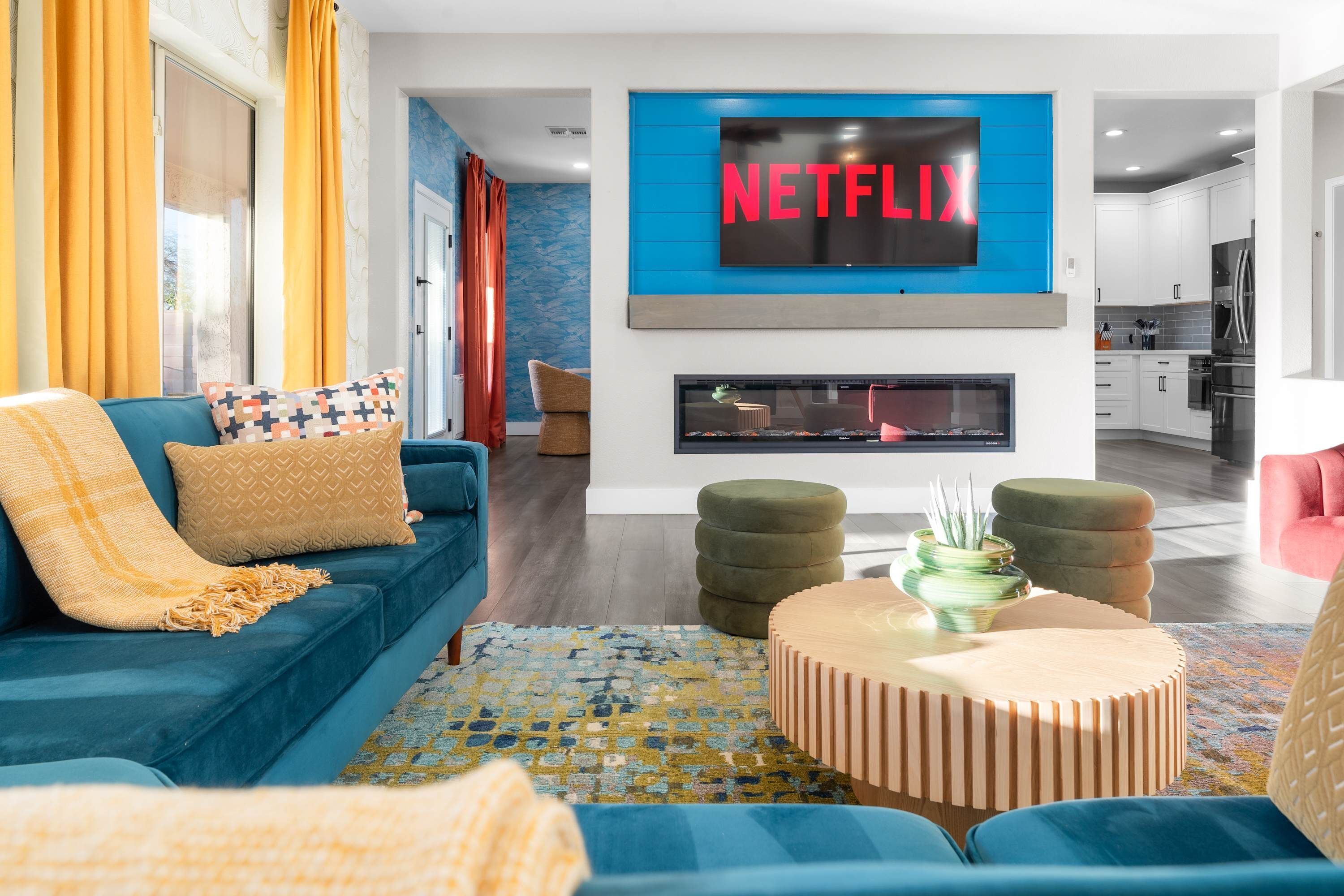Una sala de estar moderna con un sofá azul, una chimenea y un televisor montado mostrando el logotipo de Netflix.