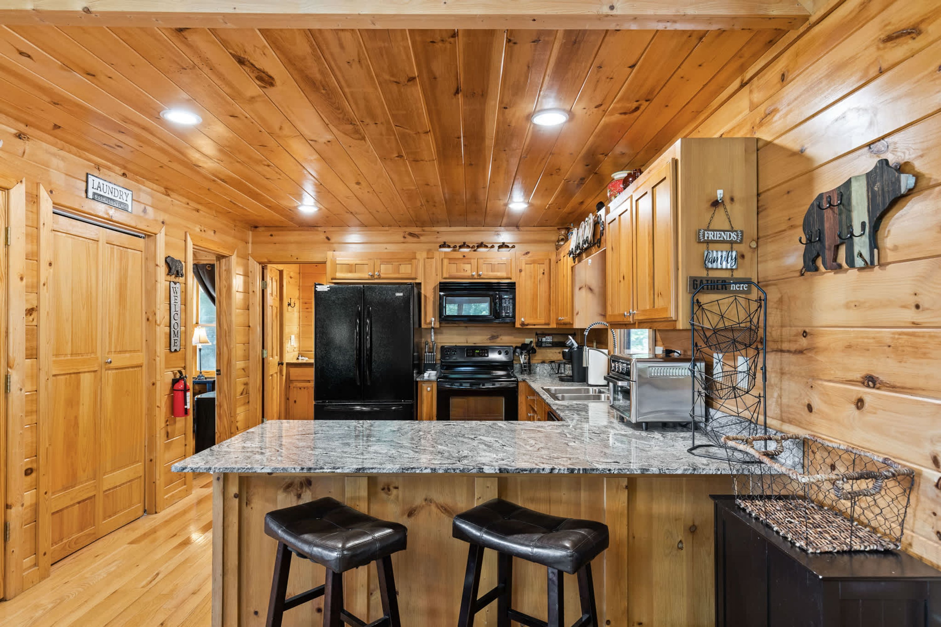 A wooden cabin interior with a kitchen area, including a refrigerator, stove, microwave, and bar stools.