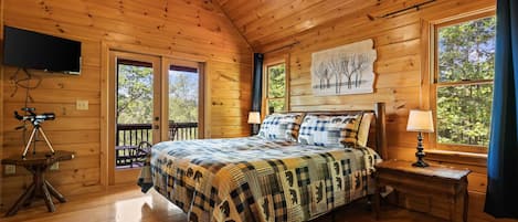 A wooden cabin bedroom with a bed, a mounted TV, and a telescope on a table.