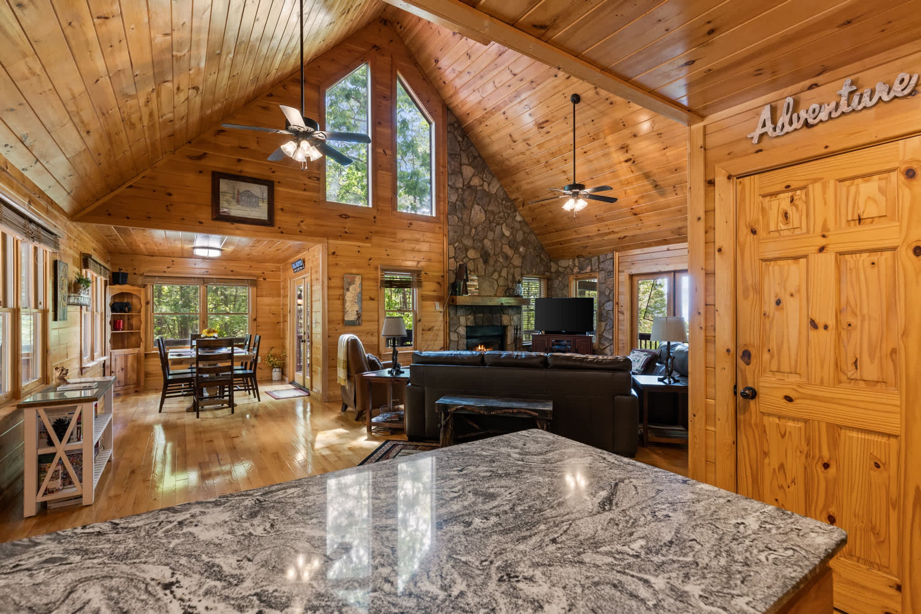 A spacious log cabin interior with a stone fireplace, a large dining table, and a bar area.