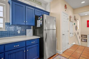 A kitchen with blue cabinets, a stainless steel refrigerator, and a tiled backsplash. - Amazing Beach Views Boardwalk to Beach Shared Pool (Port Aransas)