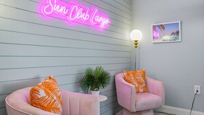 A room with two pink chairs, a neon sign reading 'Sun Club Largo', a wall-mounted light, and a framed picture. - Outdoor Movie Theatre Pool Putt Putt Hot Tub (Largo)