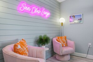 A room with two pink chairs, a neon sign reading 'Sun Club Largo', a wall-mounted light, and a framed picture. - Outdoor Movie Theatre Pool Putt Putt Hot Tub (Largo)