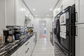 A modern kitchen with white cabinetry, a black refrigerator, and a coffee maker. - Outdoor Movie Theatre Pool Putt Putt Hot Tub (Largo)