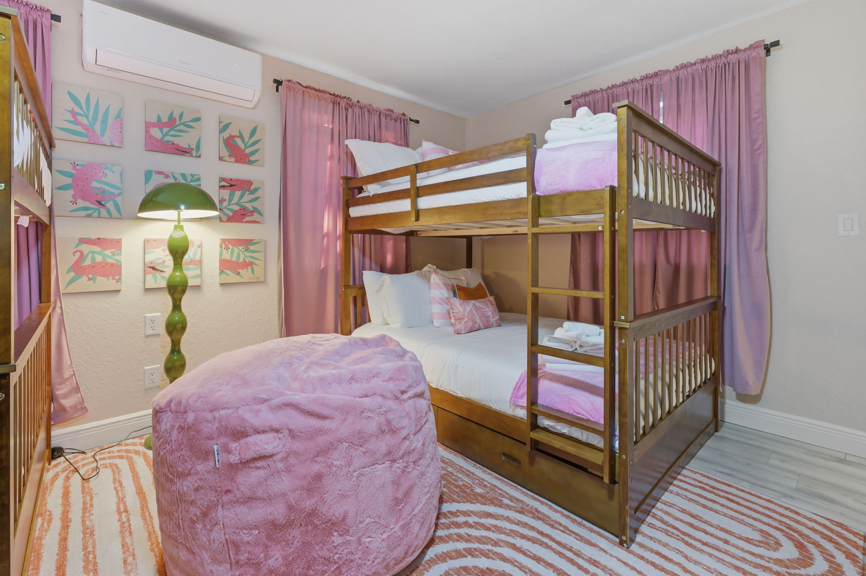 Habitación con literas, un reposapiés rosa, una lámpara y decoración en las paredes.