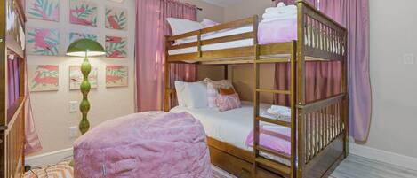 Habitación con literas, un reposapiés rosa, una lámpara y decoración en las paredes.